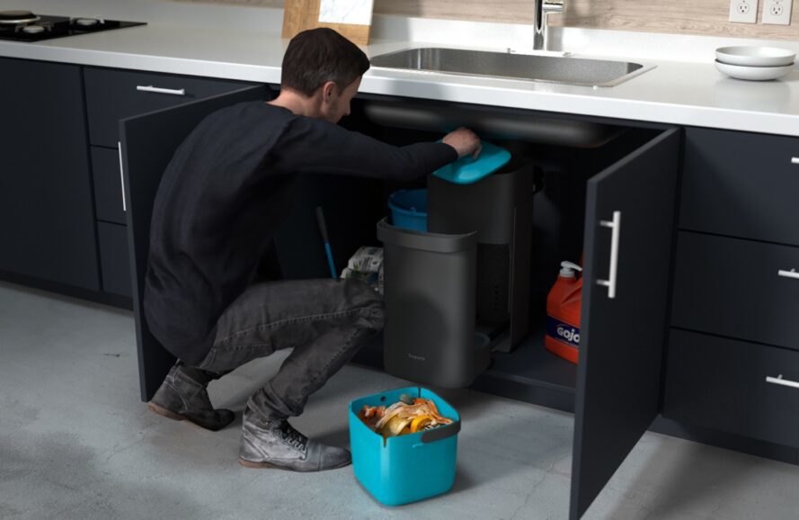 person emptying gray compost bin located under a sink