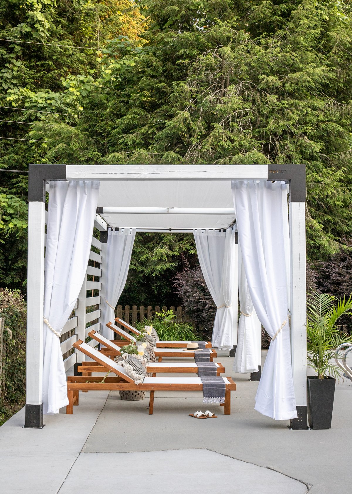 white DIY pergola cabana with outdoor curtains and lounge chairs