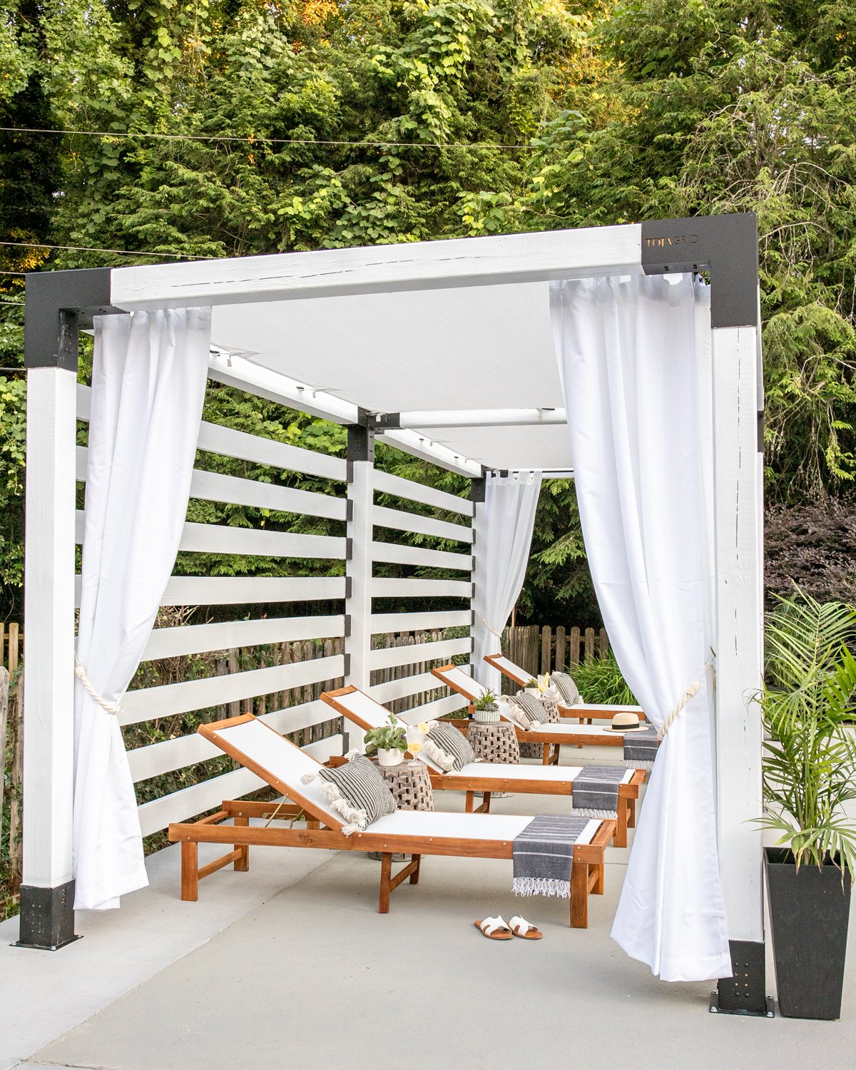 outdoor lounge chairs under a white pergola cabana with outdoor curtains