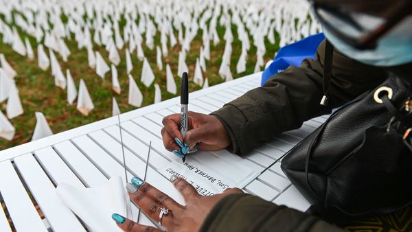 Patrice Howard writes on white flags before planting them to remember her recently deceased father and close friends in November at "IN AMERICA How Could This Happen...," a public art installation in Washington, D.C. Led by artist Suzanne Firstenberg, volunteers planted white flags in a field to symbolize each life lost to COVID-19 in the U.S.
