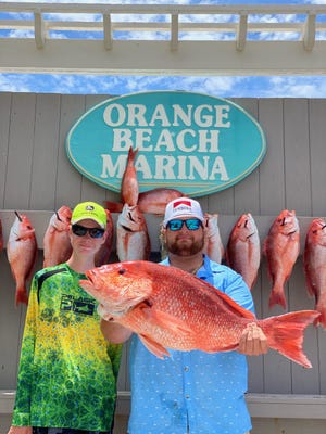 Cooper Meshew (left) stands with a family friend in Orange Beach, Alabama after Meshew caught the fish his friend is holding in June 2021. Meshew has a medical condition that limits his hand mobility but he used a fishing rod with an electric reel to catch the fish.